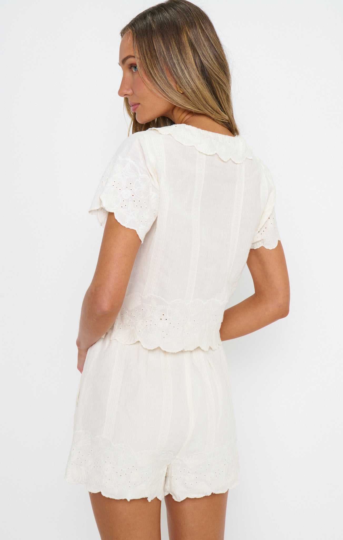 Woman in a white embroidery button up top and white scalloped shorts
