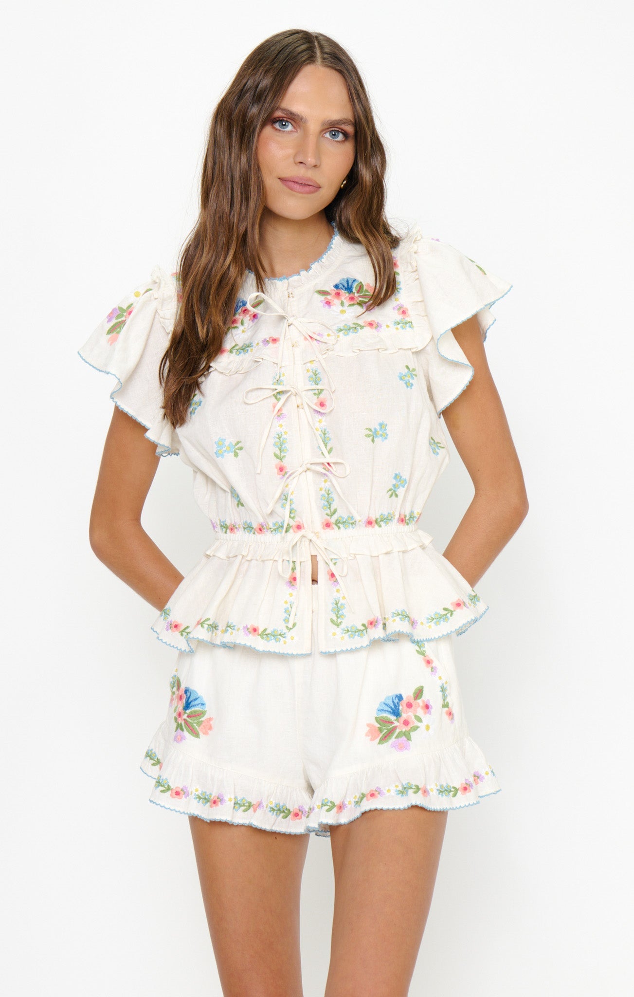 Woman in embroidered white shorts, standing against a plain background. Cotton fabric, casual summer wear.