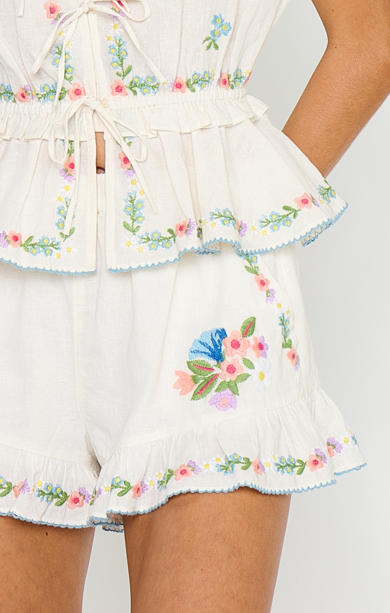Woman in embroidered denim shorts with a wild meadow motif, hand on hip. Casual wear suitable for warm weather.