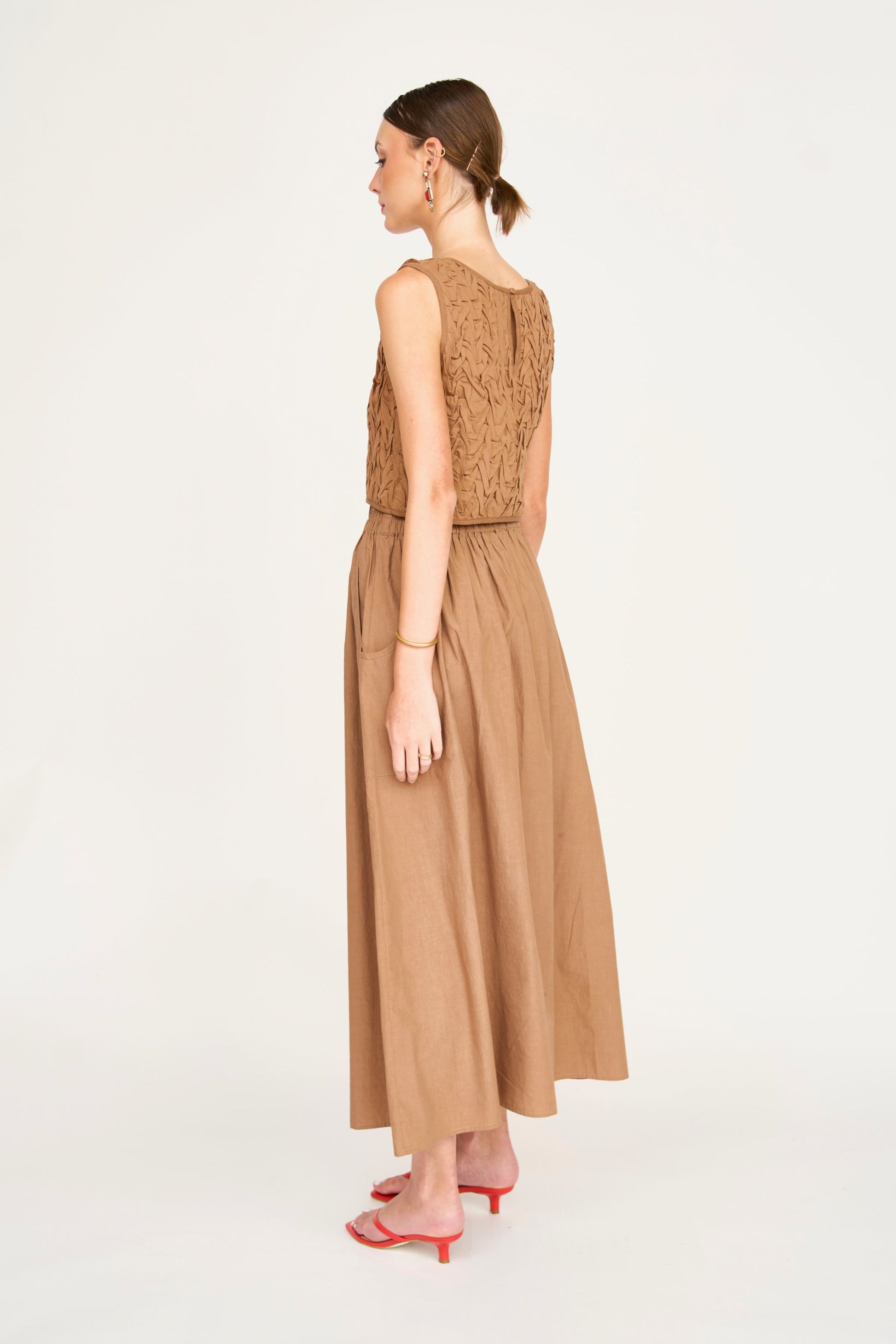 Side view of woman wearing a brown smocked top, lightweight material, styled for everyday casual use against white background.