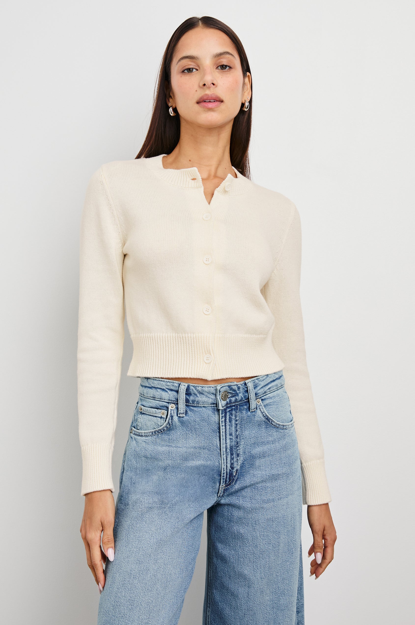 Ivory knit cardigan and blue jeans, modeled by a woman standing against a plain white background.