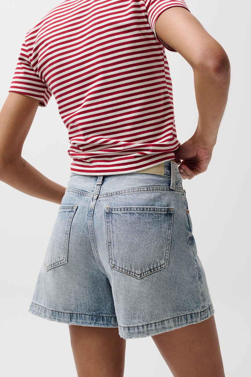 Person facing away, hands on hips, wearing light blue denim shorts suitable for casual summer wear.