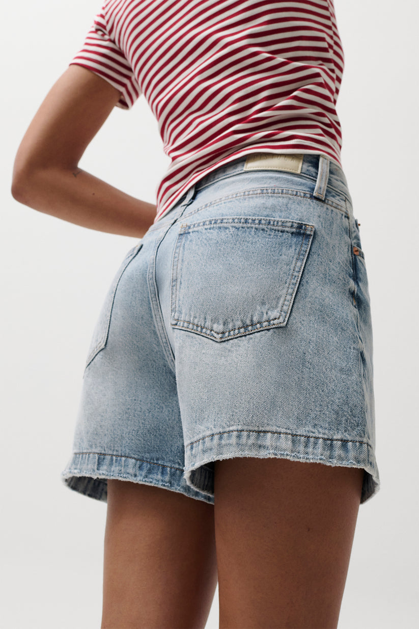Woman in denim Saige shorts, French Riviera wash, side and back view, styled with a red and white striped shirt.