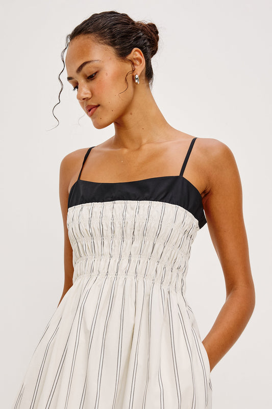 Black-and-white striped sleeveless dress with thin straps, worn by a woman with her hair in a neat bun.