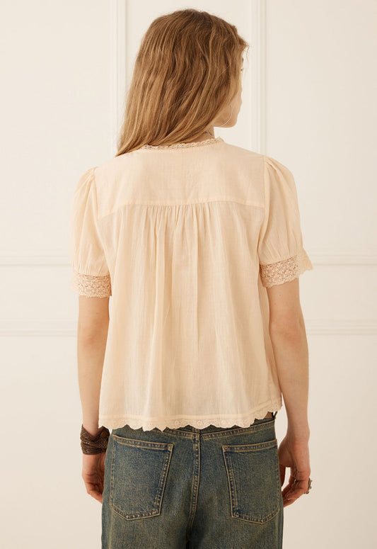 A woman wearing a light beige short-sleeve blouse with lace trim and button details