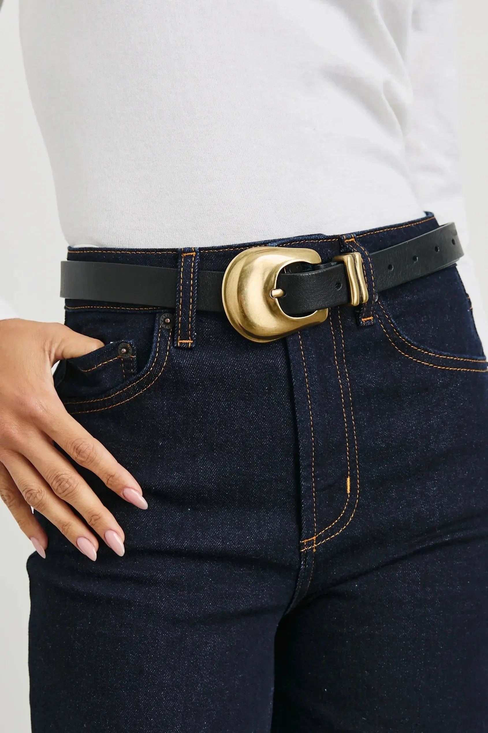 High-waisted dark blue jeans, white long-sleeve shirt, and black leather belt with gold buckle.