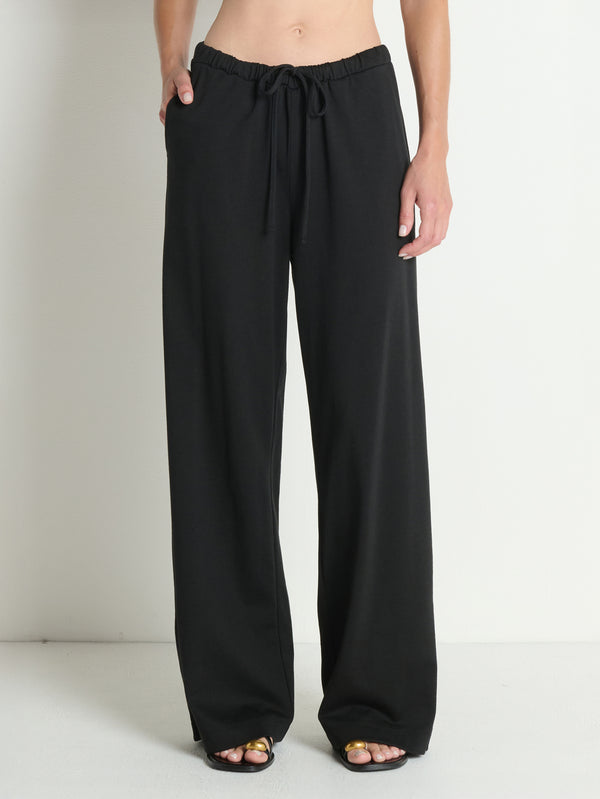 Individual in black cotton pants and open-toe sandals, standing upright against a neutral, plain background.