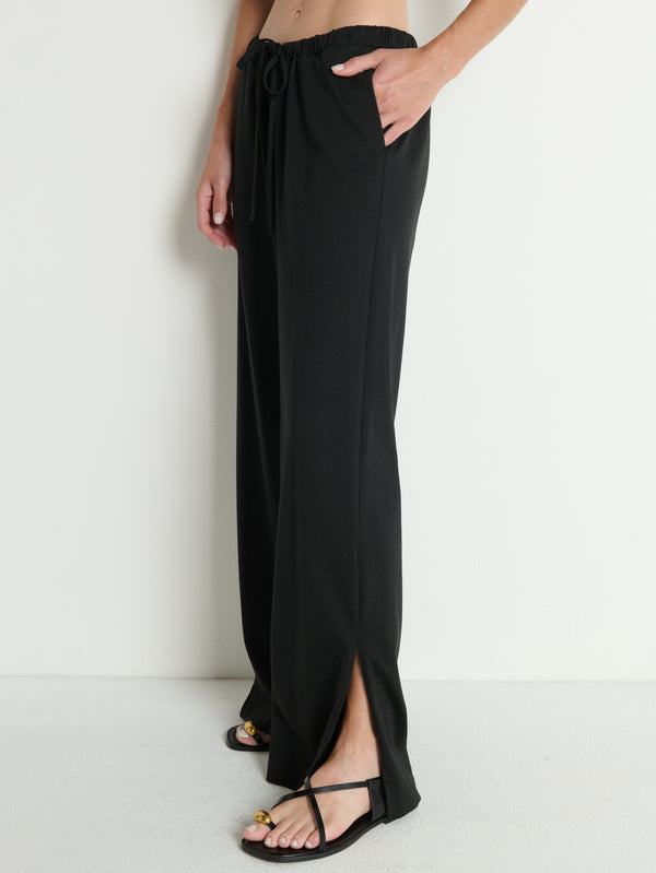 Person wearing black cotton pants and black sandals, standing against a plain white background.