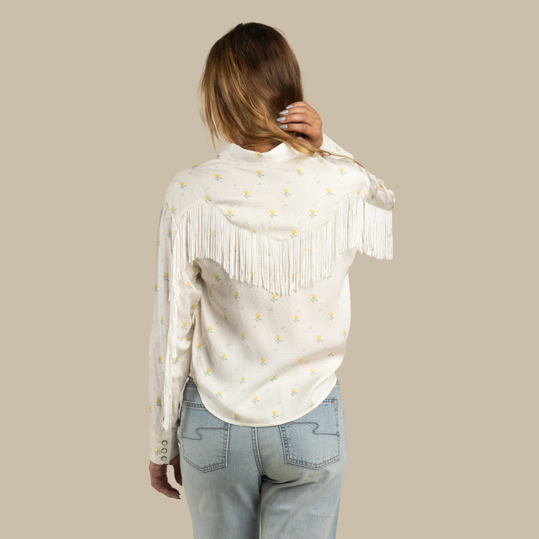 Back view of a woman wearing a Texas rose print blouse and light blue denim jeans.
