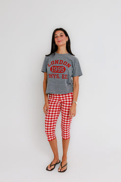 Woman in a white crew neck tee, red gingham leggings, and flip-flops stands against a plain white background.