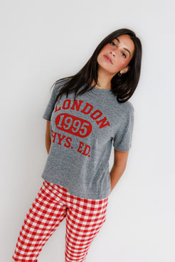 Woman wearing a gray crewneck sweatshirt and red plaid pants, standing against a plain white background.