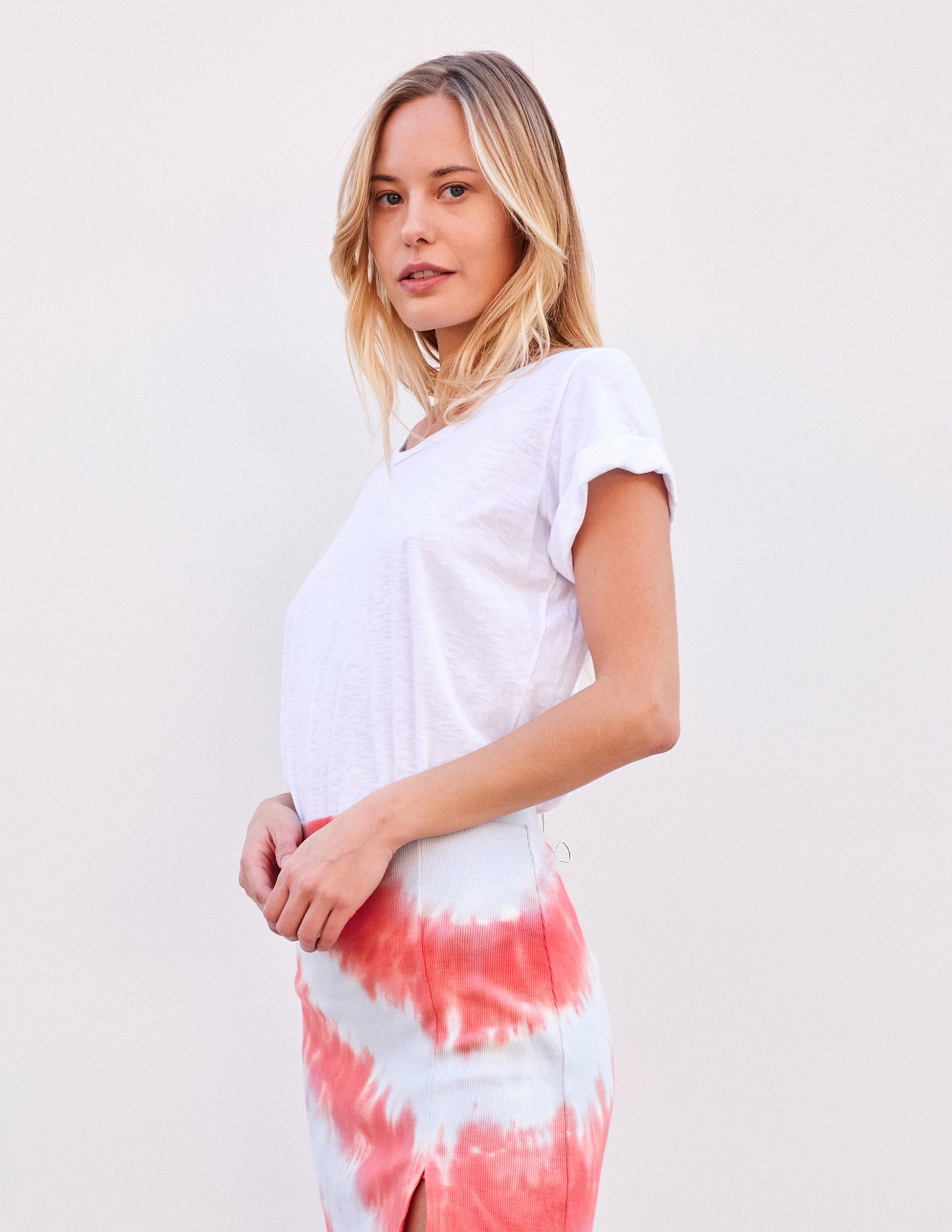 Woman in white rolled-sleeve tee and red-and-white tie-dye skirt, cotton, on plain backdrop. Made in USA.