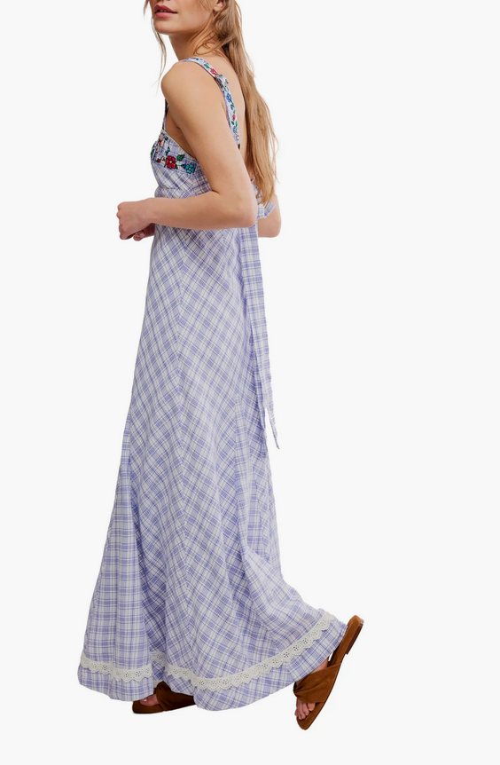 Woman wears a white patterned maxi dress and brown sandals, walking sideways; lightweight fabric ideal for warm weather.