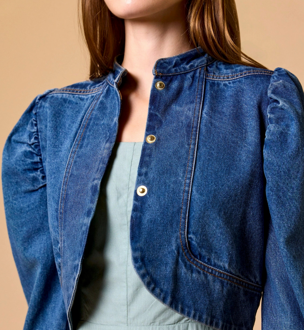 Woman in medium denim jacket over light green top, standing against a neutral background.