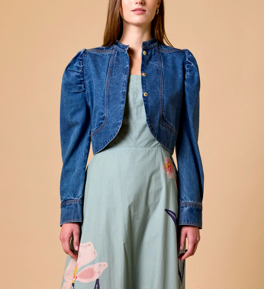 Woman in medium denim jacket over a light green floral dress, standing against a beige background.