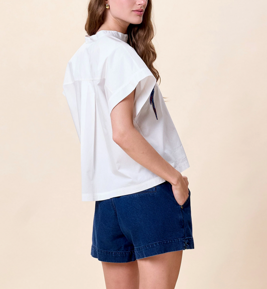 Woman in a white cotton blouse and blue denim shorts, standing with one hand in her pocket.