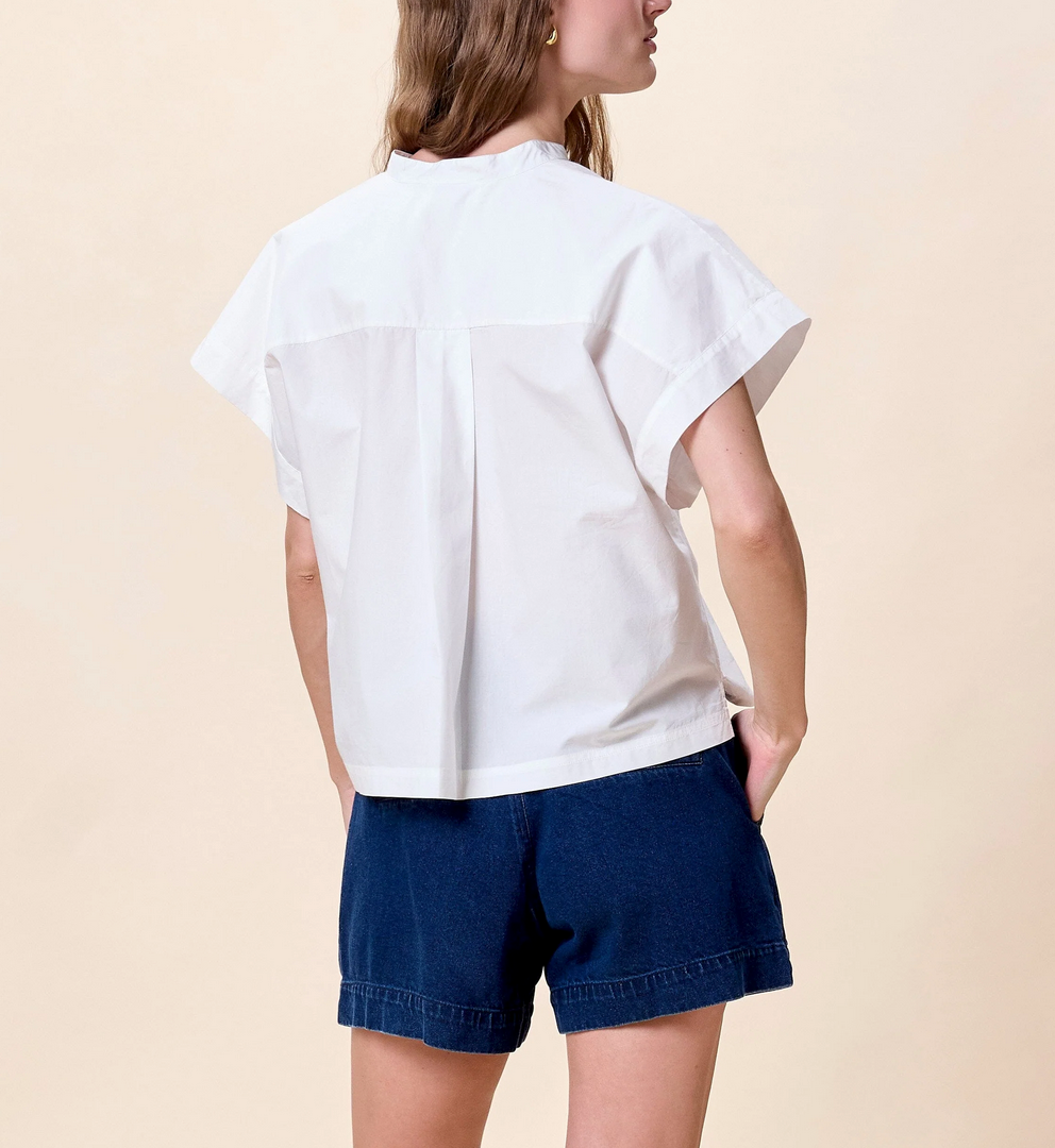 Woman with back turned, hands in pockets, wearing a white blouse and dark blue shorts.