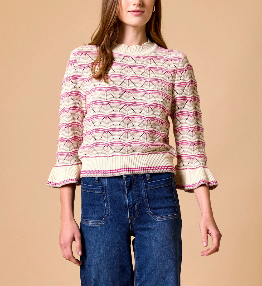 Ivory sweater with pink patterns and ruffle cuffs, paired with high-waisted blue jeans; suitable for casual wear.