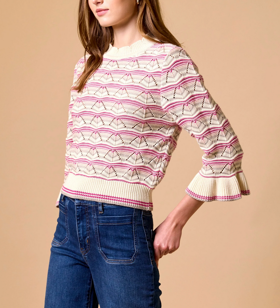 Cream and pink knit sweater with ruffle cuffs, paired with blue jeans; worn for casual or everyday use.