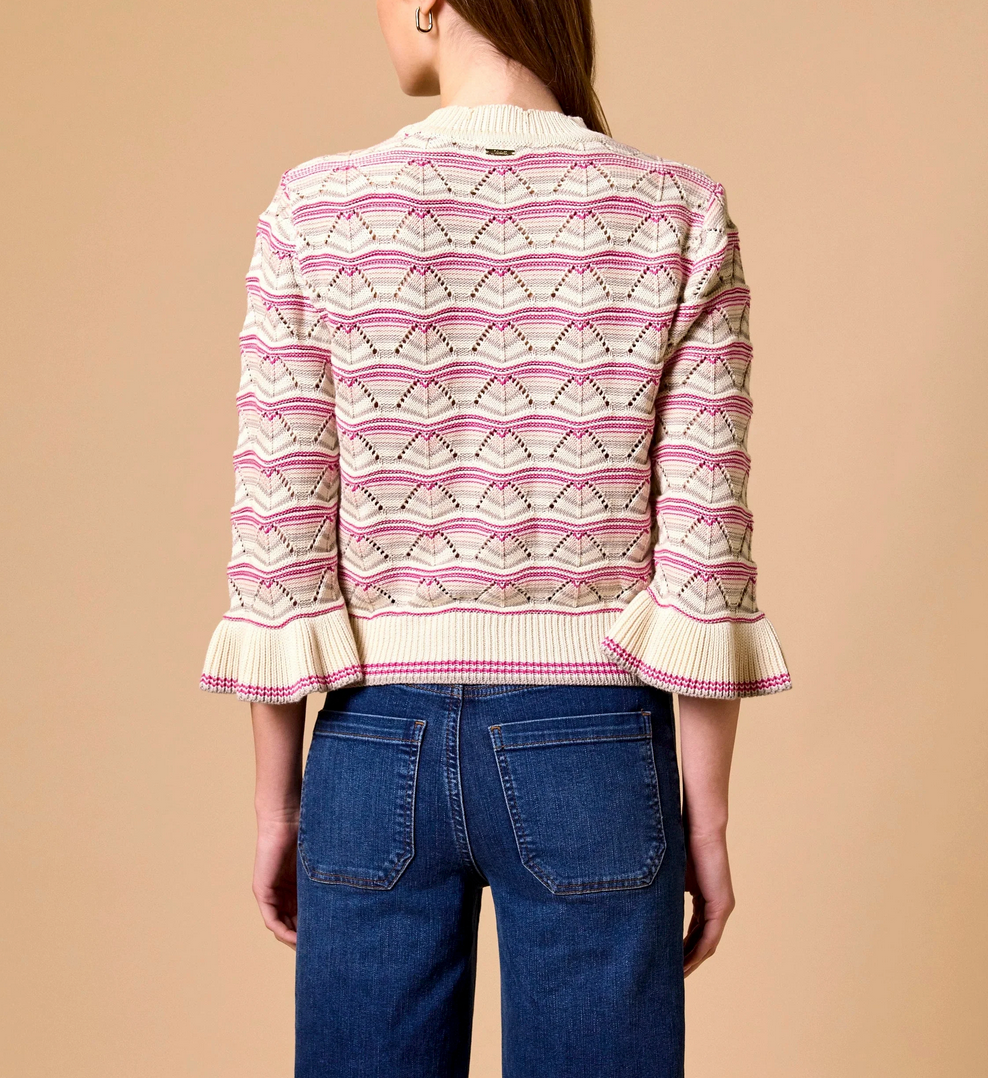 Back view of woman in blue jeans and an ivory multi-colored knit sweater against a beige background.