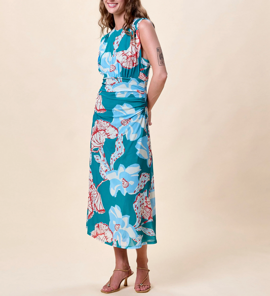 Woman wearing a patterned midi dress and heeled sandals stands against a beige background.