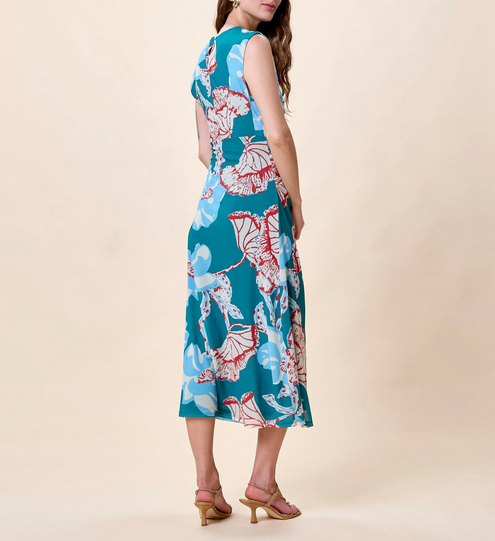 Woman in a printed midi dress with red and blue patterns stands with her back turned, looking over her shoulder.