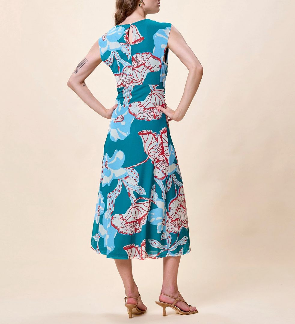 Woman in a patterned midi dress stands with her back to the camera against a beige background.