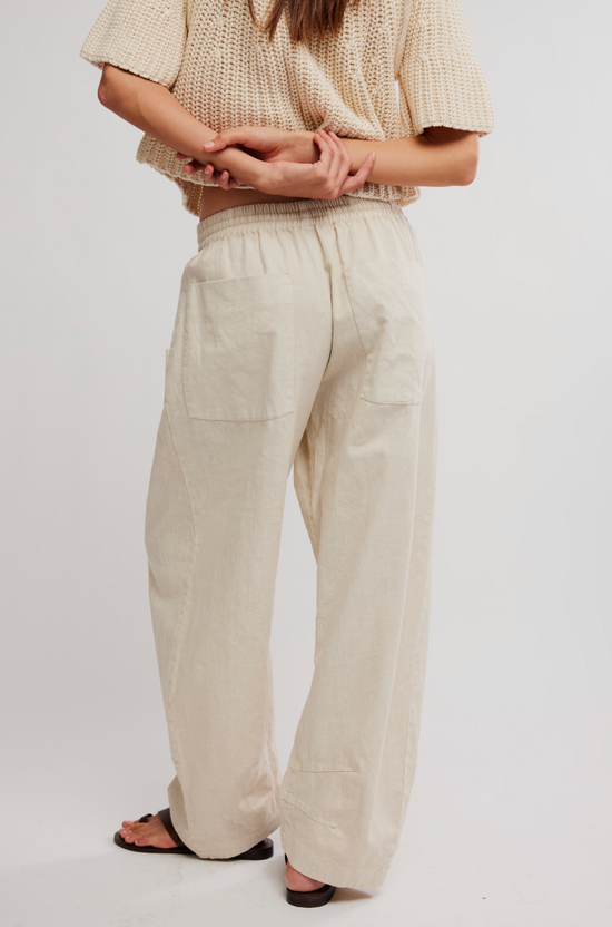 Barefoot woman wearing light beige pull-on pants, relaxed fit, hands behind back. Suitable for casual wear.