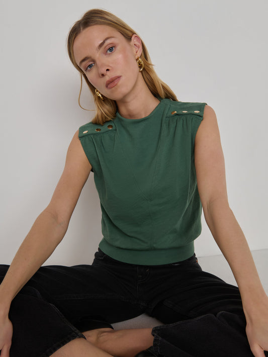Woman in a sleeveless floral top and black pants sits cross-legged against a plain white background.