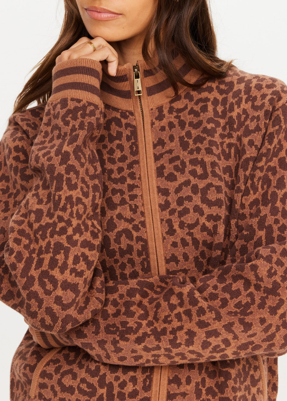 Woman in a leopard print knit jacket with hand near face, showcasing the garments pattern and texture.