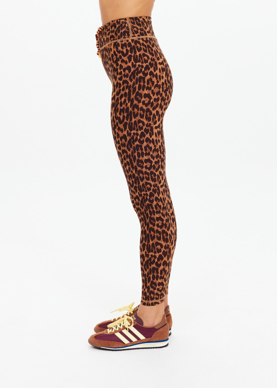 Side view of person in leopard-print midi pants and maroon sneakers with yellow laces, standing against a white background.