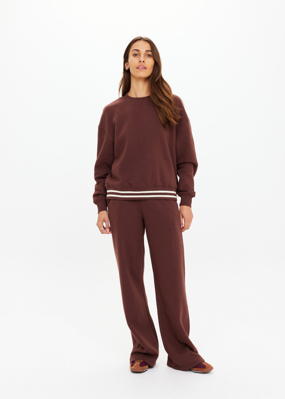 Woman in cocoa crew neck sweater and matching pants, likely cotton blend, standing against plain white background.