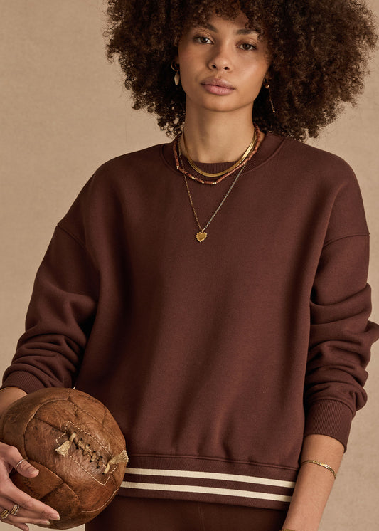 Woman in cocoa crew neck sweater holds a vintage leather basketball, accessorized with gold jewelry.