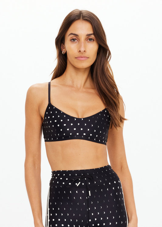 Woman with long brown hair models a black sports bra against a white background, highlighting its fit and athletic use.