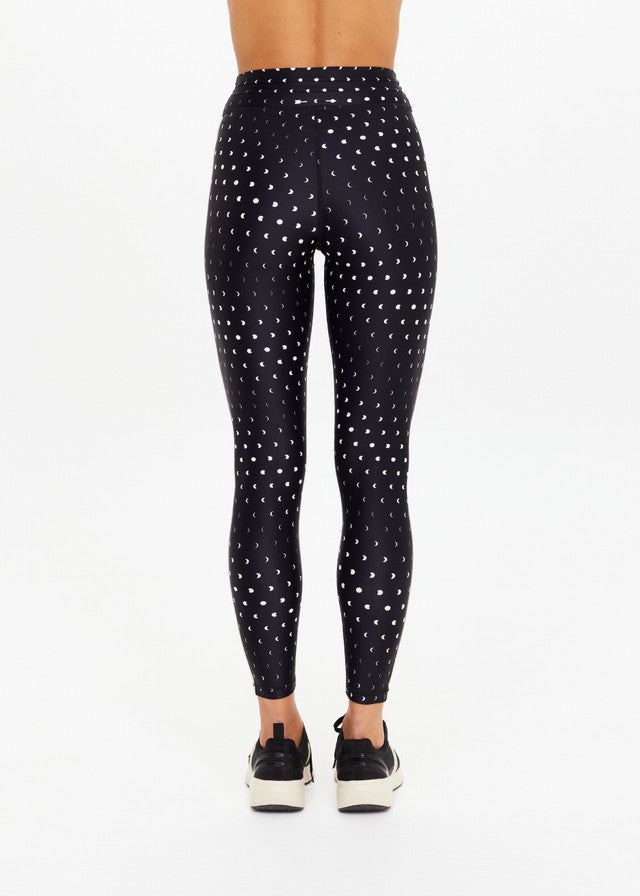 Black midi pants with white dots, worn with black sneakers; crafted from recycled soft fabric for active or casual wear.