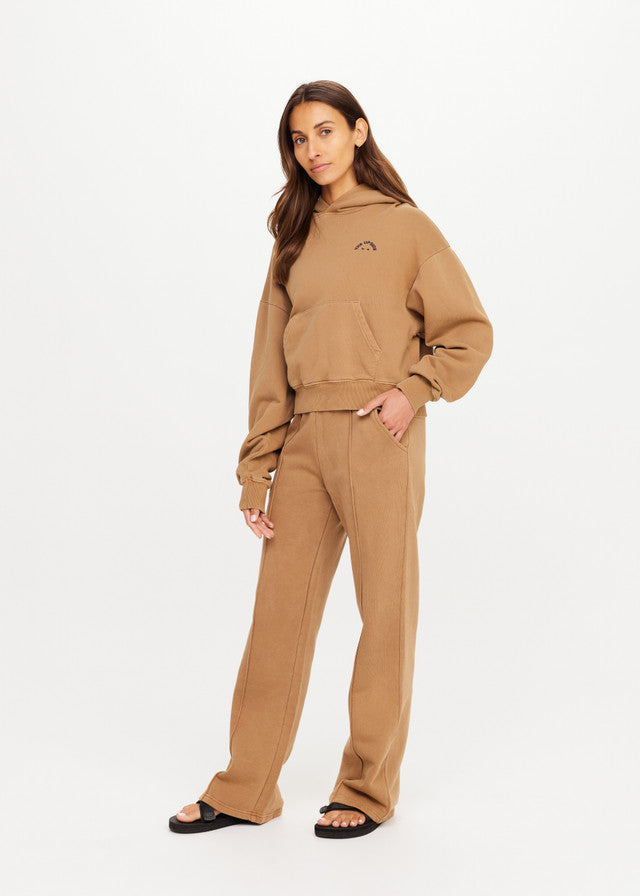 Woman in chai-colored hoodie and matching pants with black sandals, shown against a plain white background.