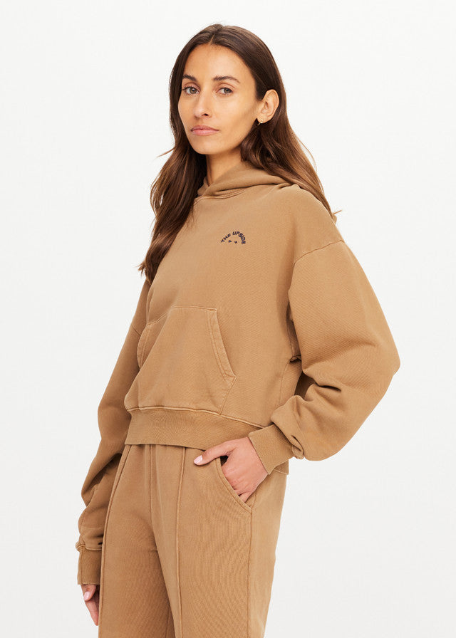 Woman in chai-colored hoodie, soft fabric, for casual wear, stands facing camera against a plain white backdrop.