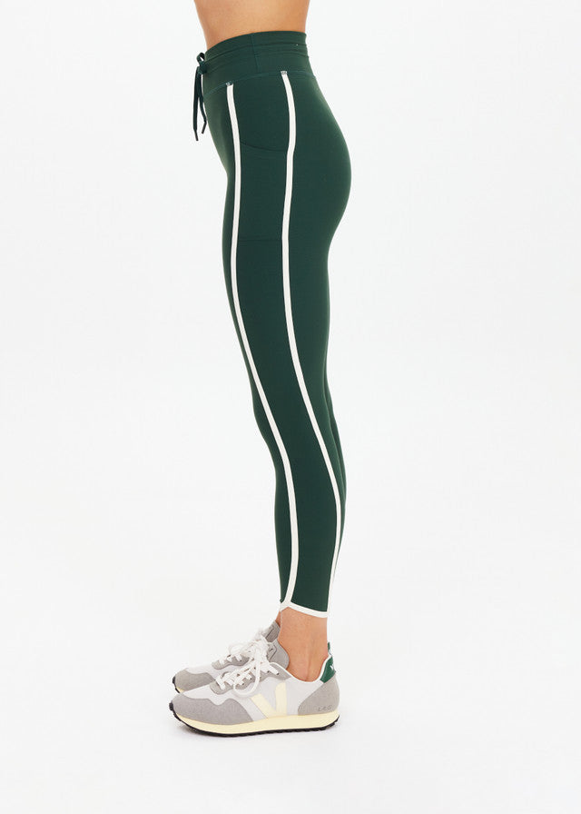 Side view of green midi athletic pants with white stripes, paired with gray sneakers.