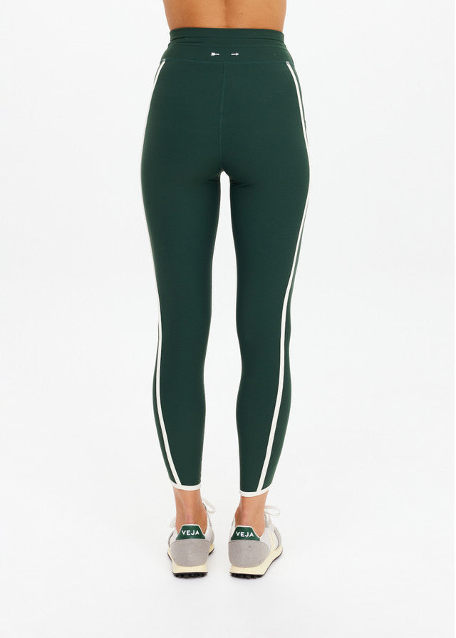 Back view of green midi athletic pants with white side stripes, paired with beige sneakers.