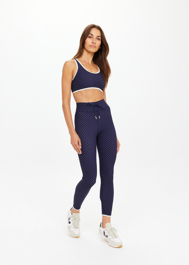 Woman wearing black polka dot midi pants, lightweight fabric, ideal for casual or active wear, standing against white background.