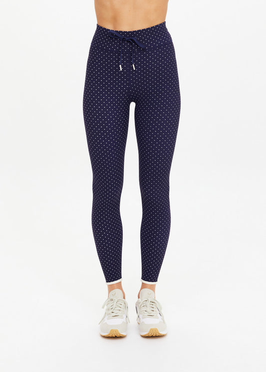 Woman in black polka dot cropped leggings with white sneakers, shown against a plain white background.