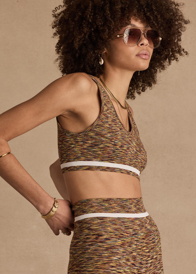Woman wears a multicolored seamless daisy bra and skirt with sunglasses, earrings, and gold jewelry.
