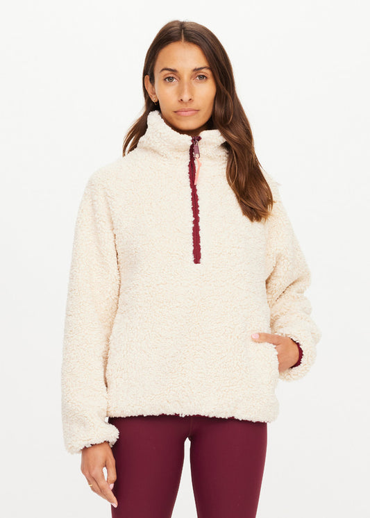 Woman in a macadamia-colored fleece pullover and maroon leggings, standing against a white background.