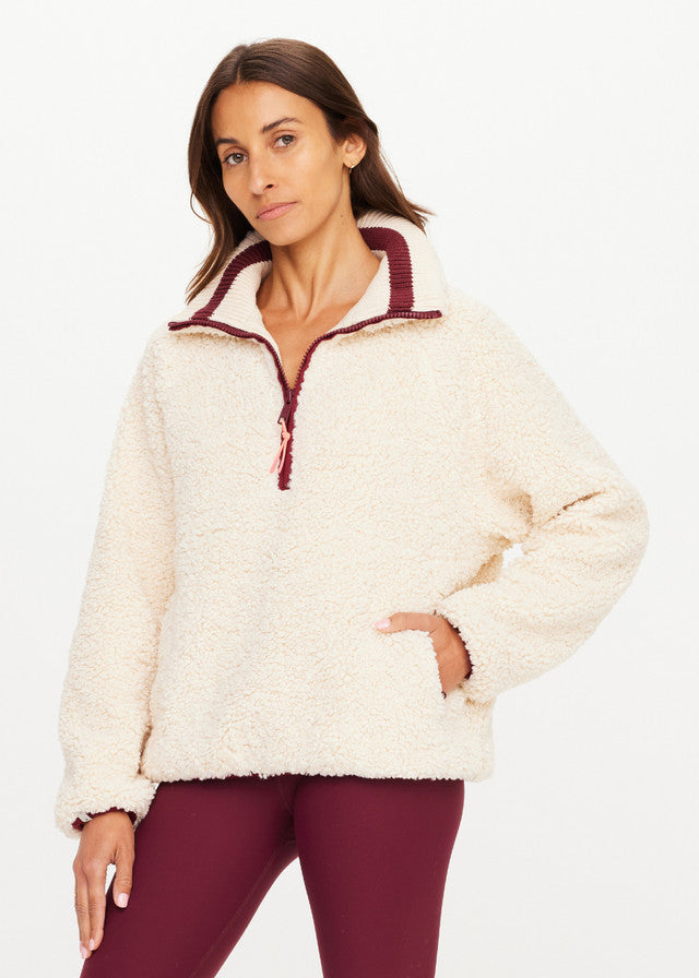 Woman in macadamia fleece pullover and burgundy leggings, standing against a plain white background.