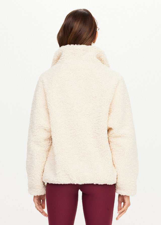 Back view of woman in macadamia fleece pullover and burgundy pants on white background; cozy, casual wear.