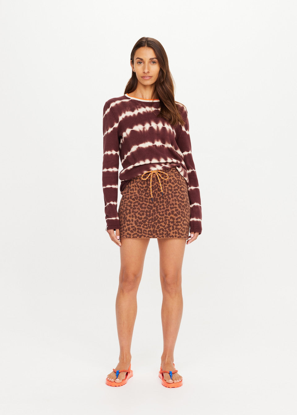Woman wears maroon tie-dye sweater, leopard-print knit mini skirt, and pink sandals against a white background.