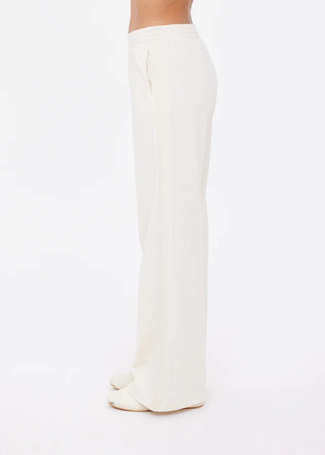Cream wide-leg pants in soft fabric, shown from the side with heels against a plain white background.