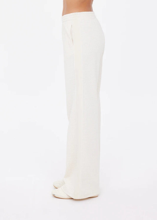 Cream wide-leg pants in soft fabric, shown from the side with heels against a plain white background.