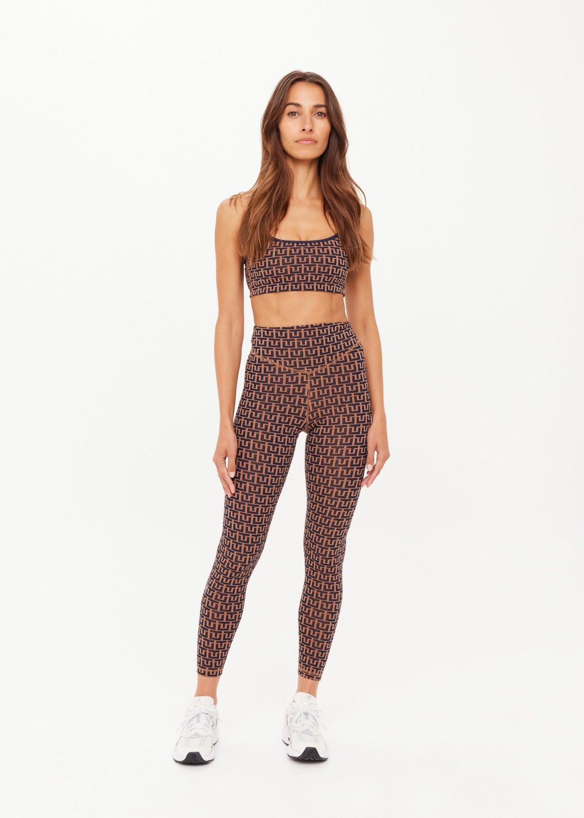 Woman in camel sports bra and matching leggings, front-facing, with white sneakers; athletic wear for workouts.