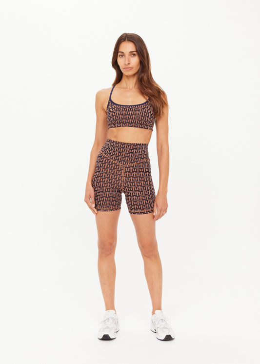 Woman in camel bike shorts and white sneakers stands against a white background.